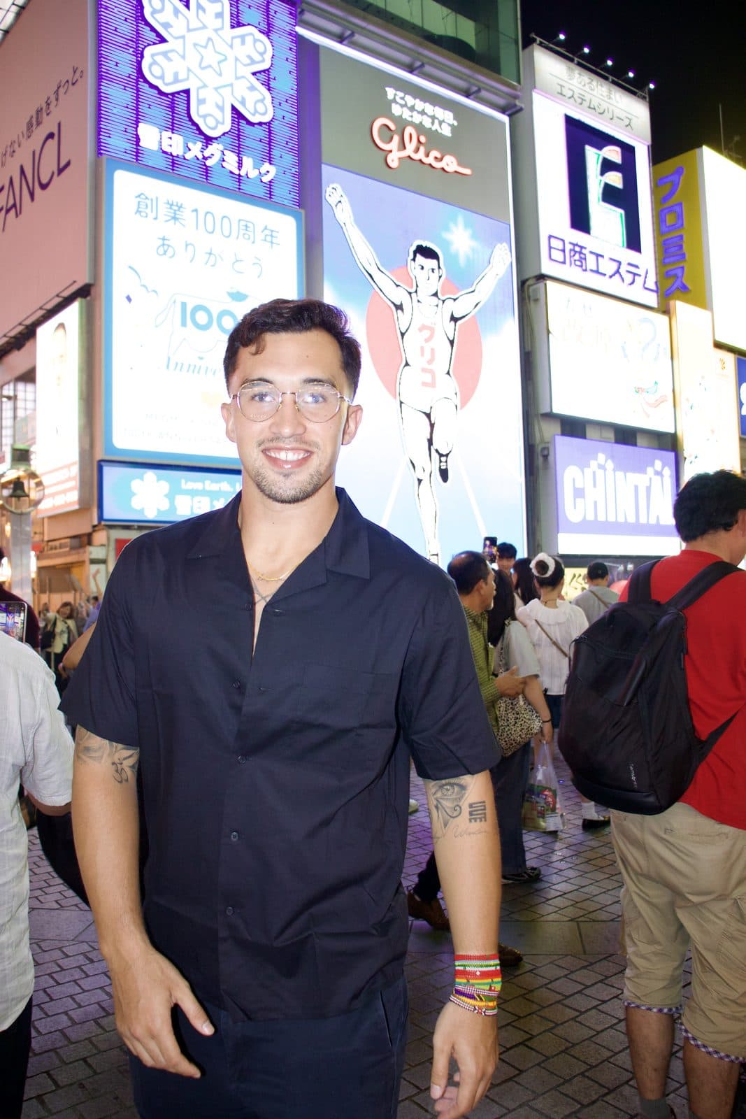 Ezekiel Contreras-Forrest in the Dotonbori district of Osaka, Japan, at night, with the street's illuminated signs and crowds behind him